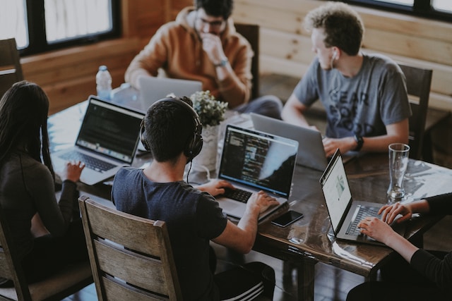 Digital native collega's werken op hun laptop samen aan een grote tafel